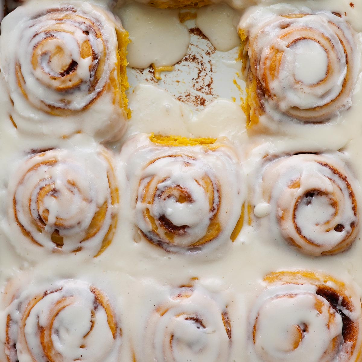 Pumpkin cinnamon rolls, frosted, in a pan, with one missing.
