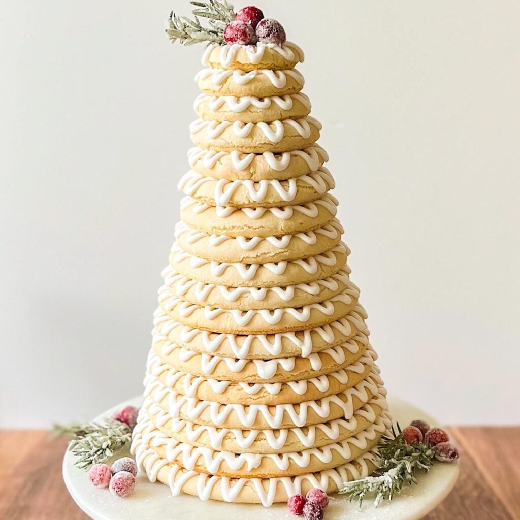 A kransekake decorated with sugared rosemary and cranberries, resting on a cake stand.