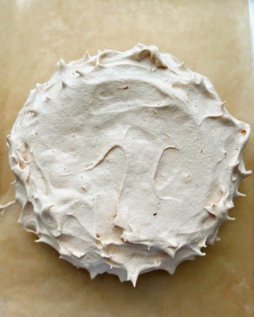 A baked pavlova on a piece of baking parchment.