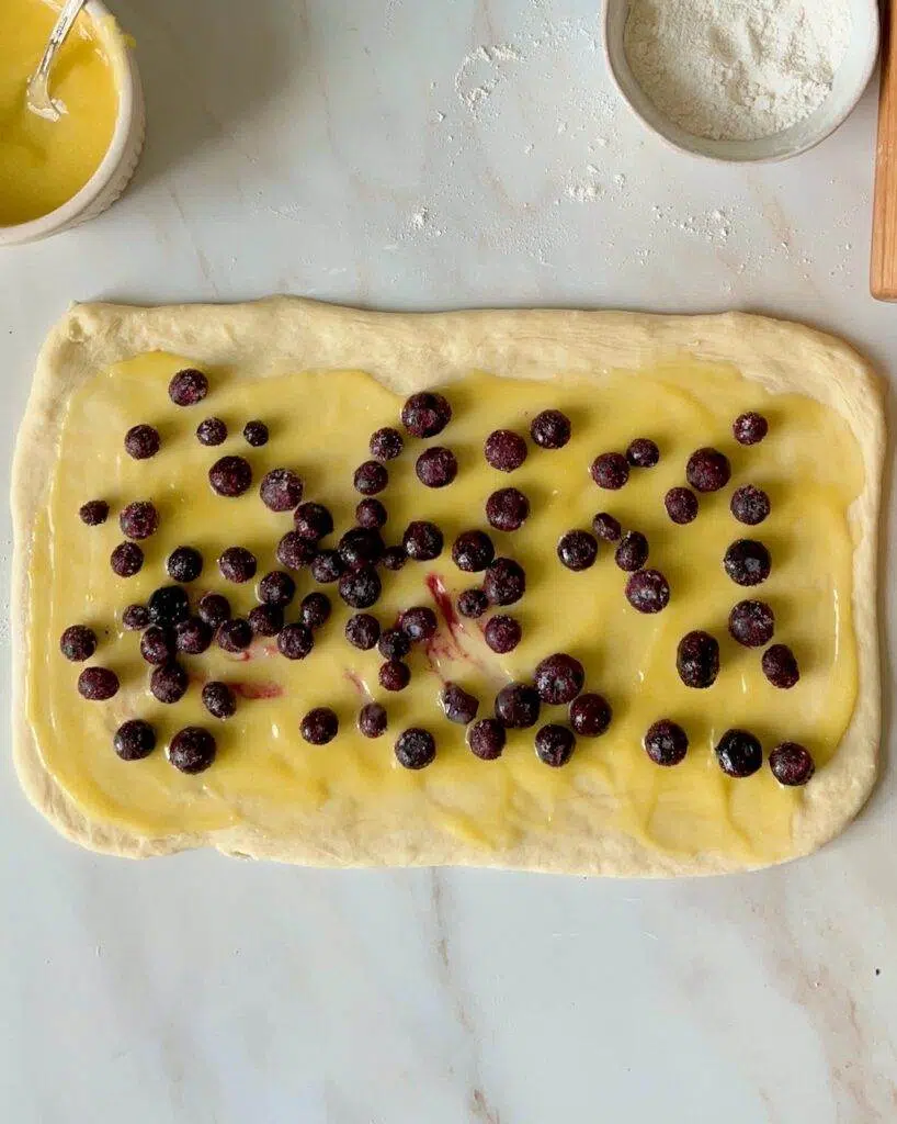 Sweet roll dough rolled out to a rectangle, with lemon curd and blueberries on top of it.