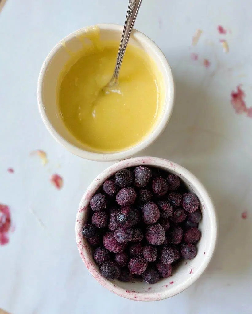A bowl of lemon curd with a spoon in it, and a bowl of blueberries.