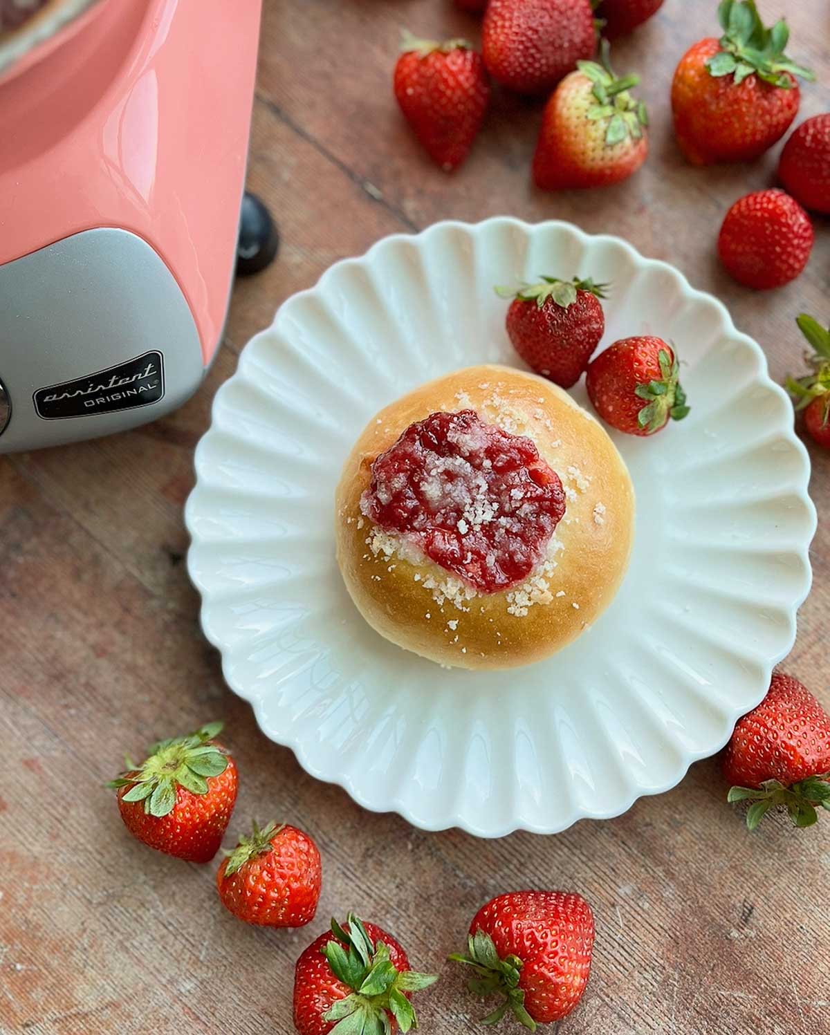 A strawberry cream cheese roll on a plate with strawberries also on the plate and around it.