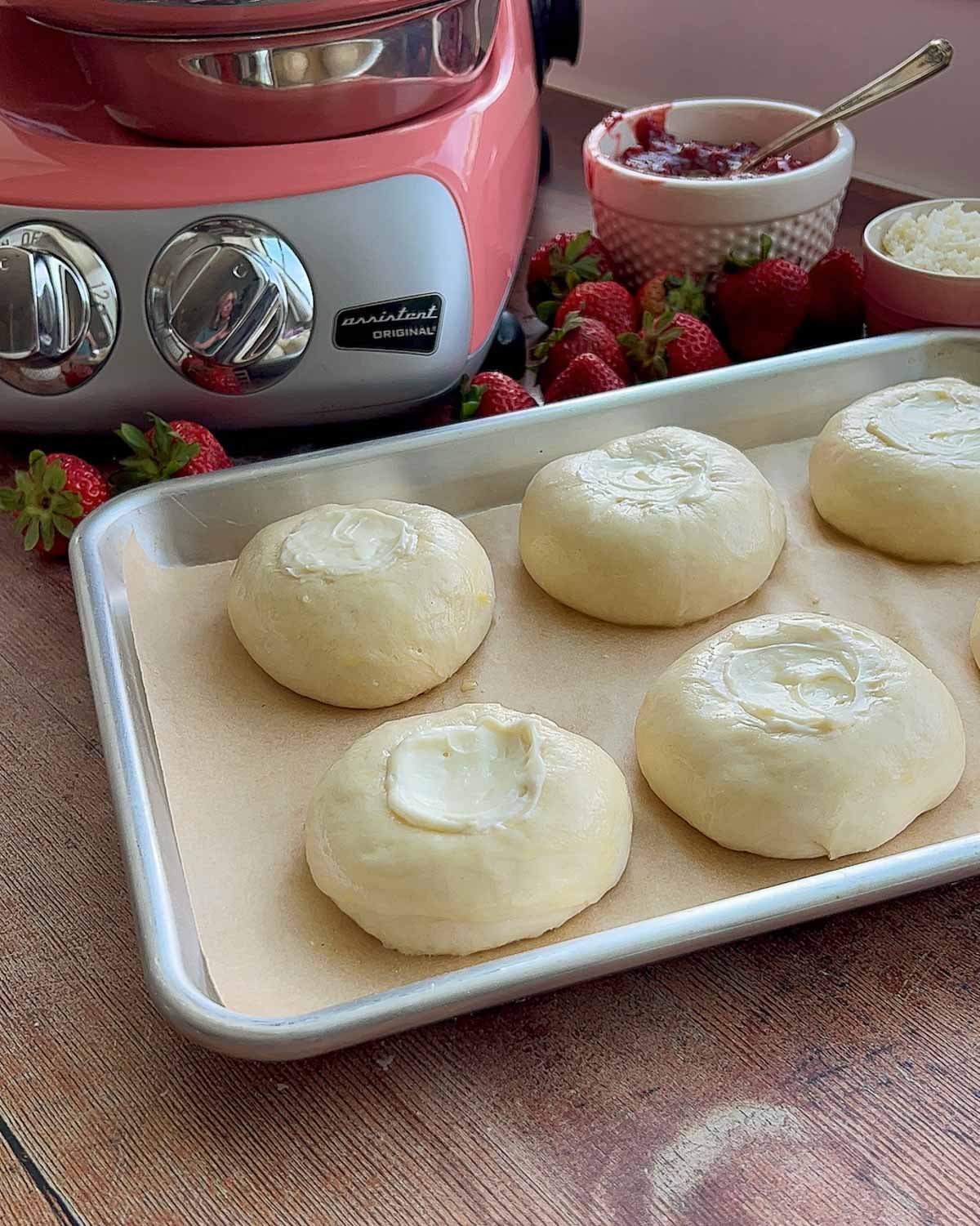 A pan of unbaked rolls with cream cheese filling in the center.