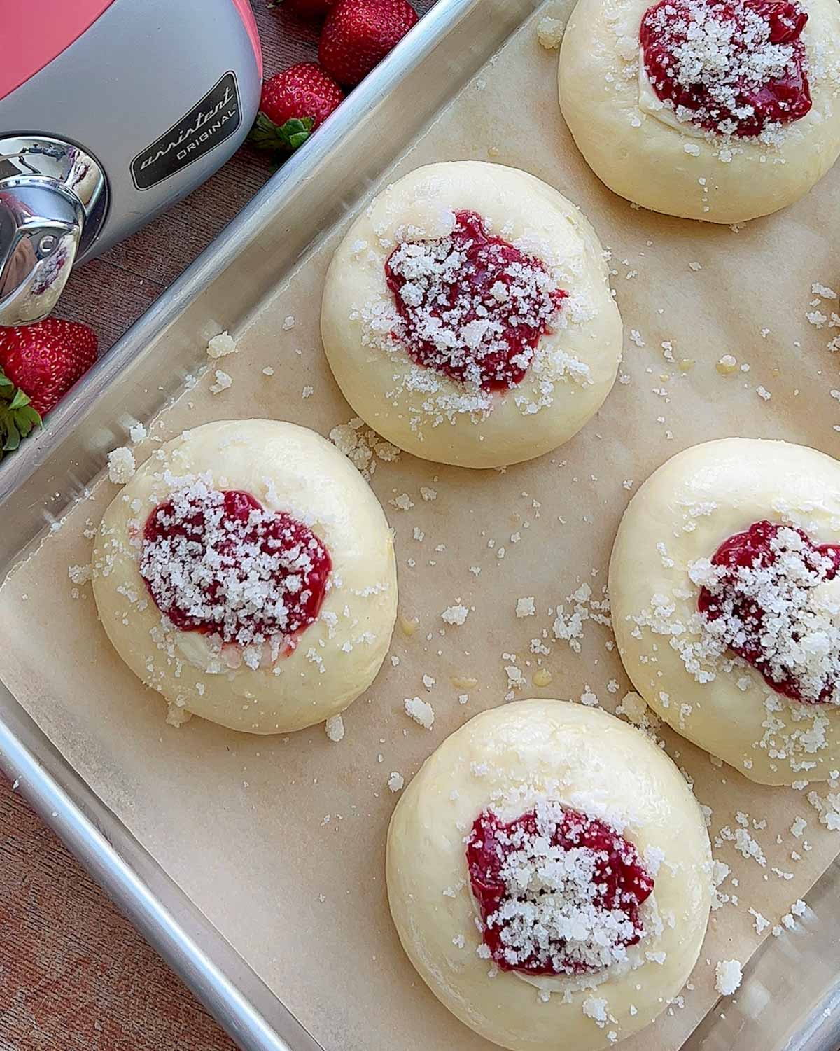 Strawberry cream cheese rolls, unbaked, with filling and crumb topping, on a pan lined with parchment.