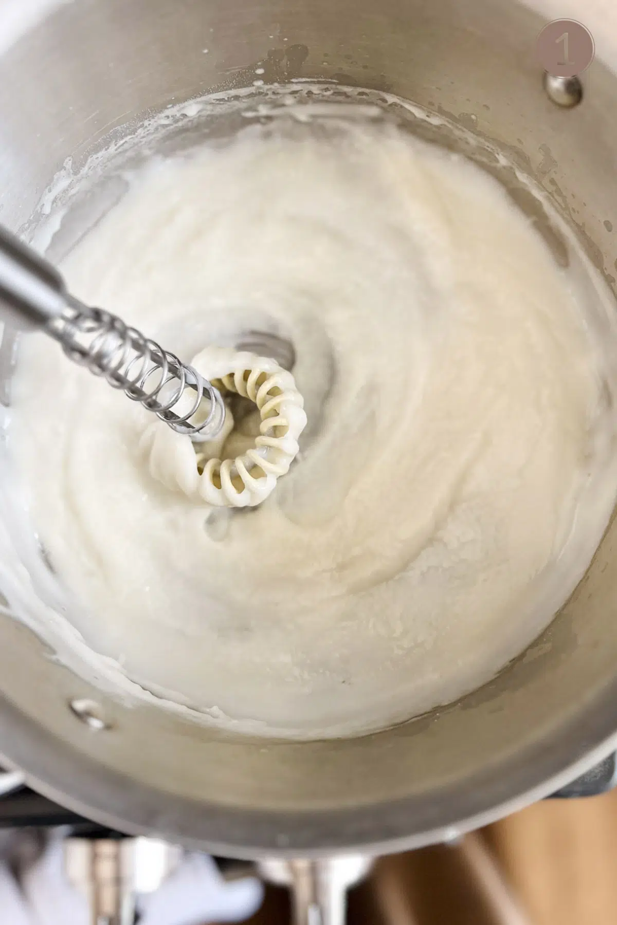 A sauce pan with a white slurry mixture inside and a flat bottom wire whisk stirring it.