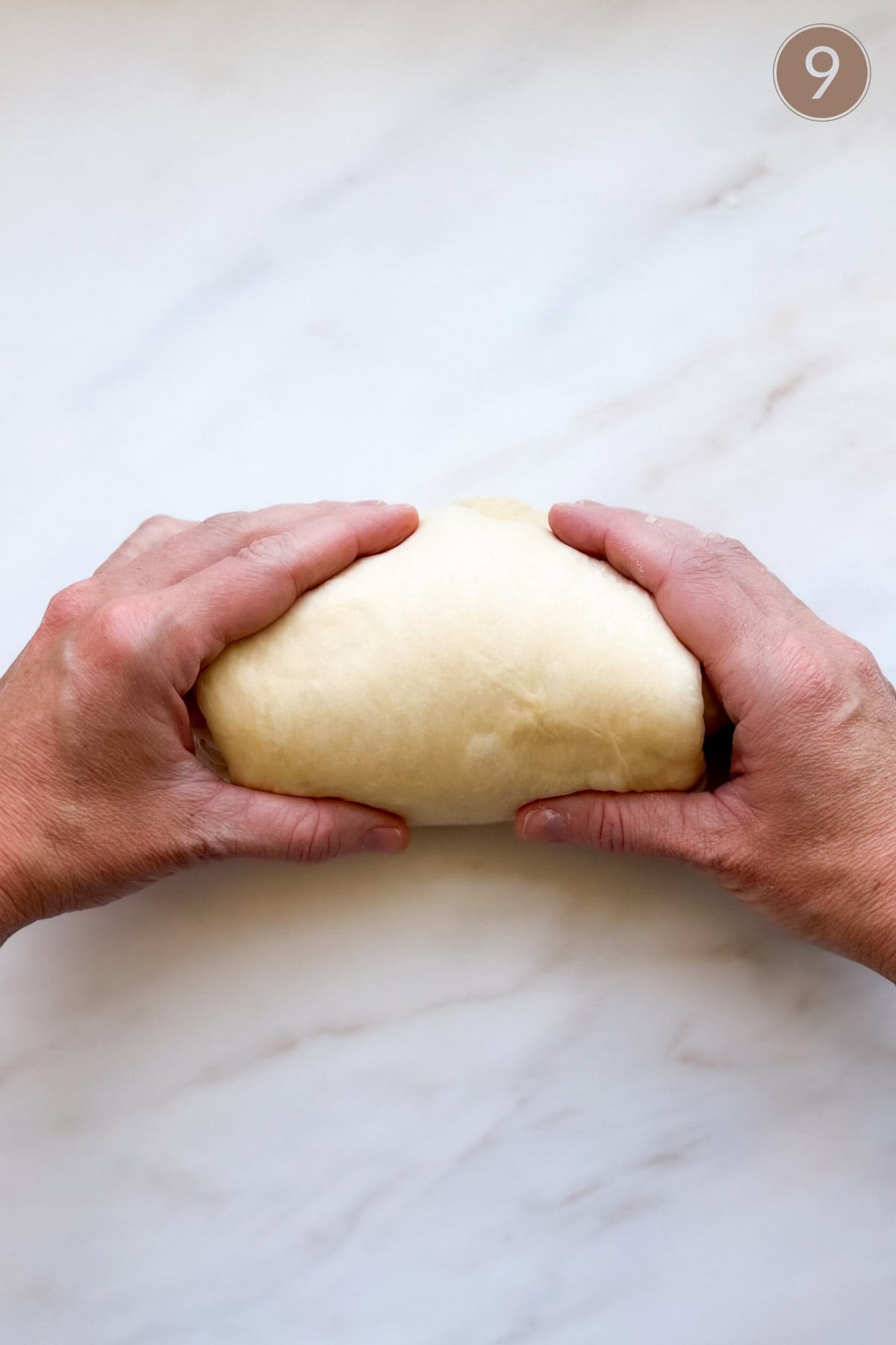 Two hands forming a loaf with bread dough.