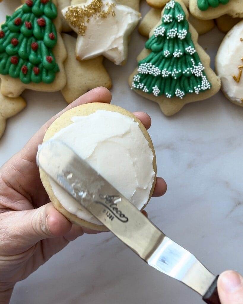 Smoothing buttercream frosting over a round shaped sugar cookie.