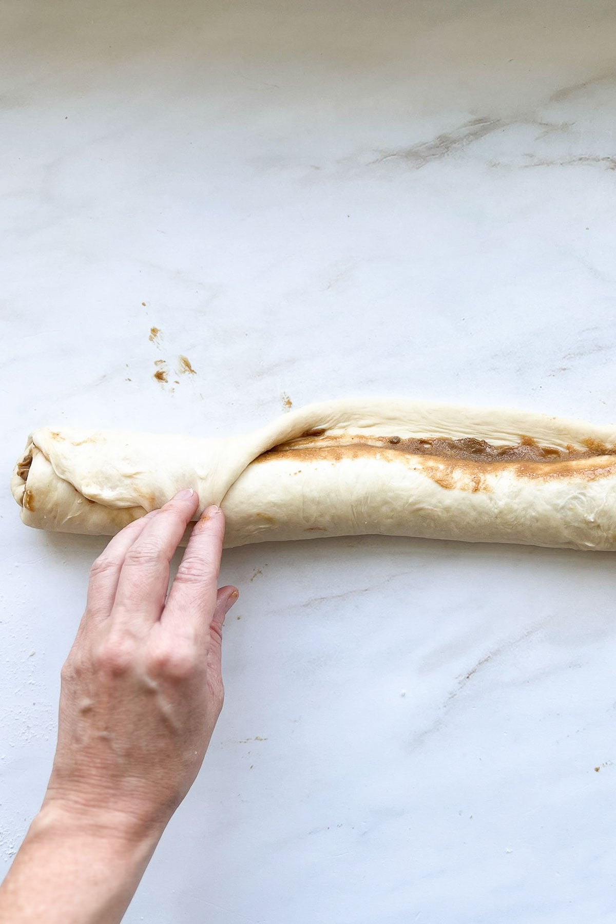 A roll of biscoff cinnamon roll dough, filled and rolled into a log, with a hand closing the end seam.