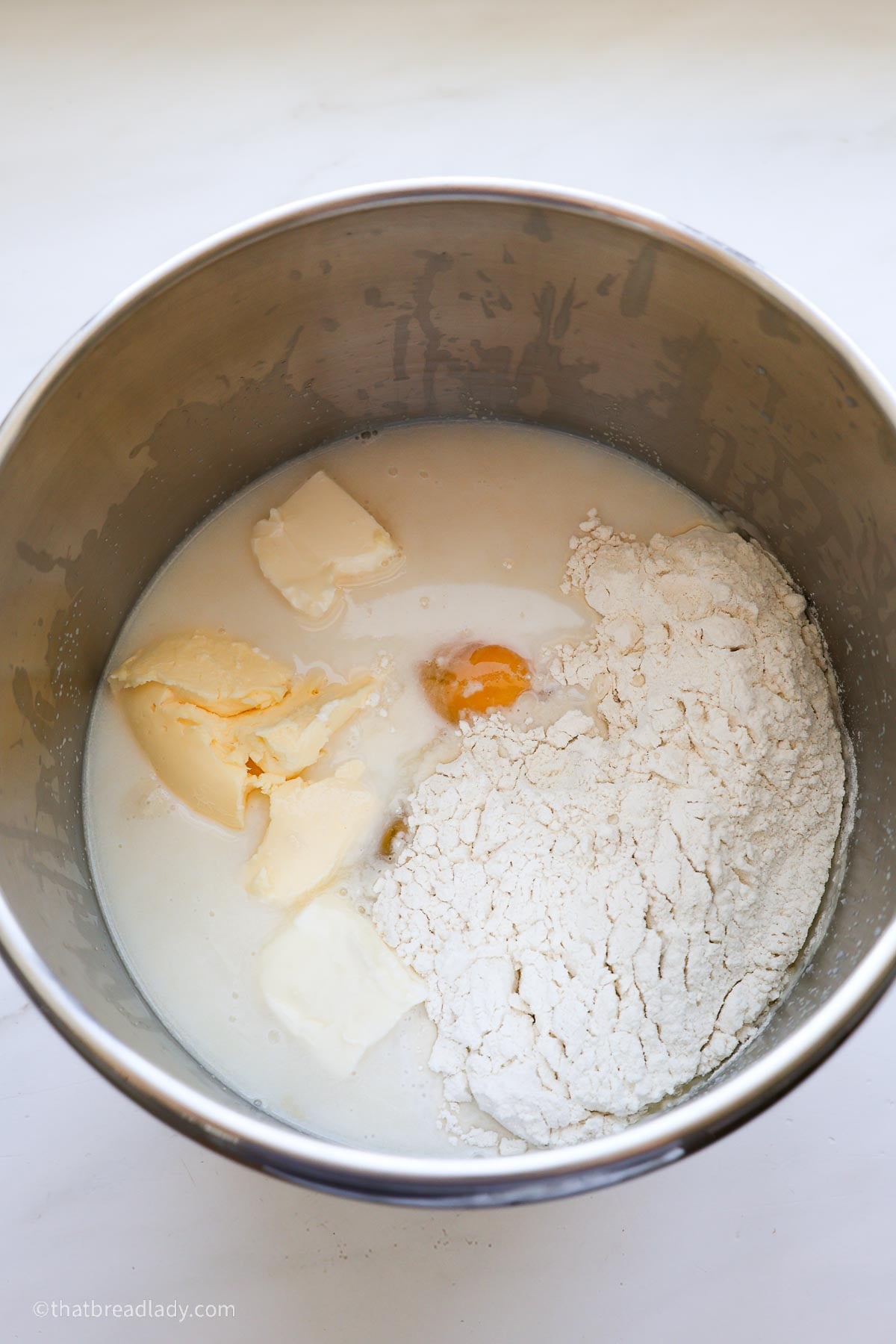 A stainless steel mixer bowl with the unmixed ingredients for Biscoff cinnamon rolls.