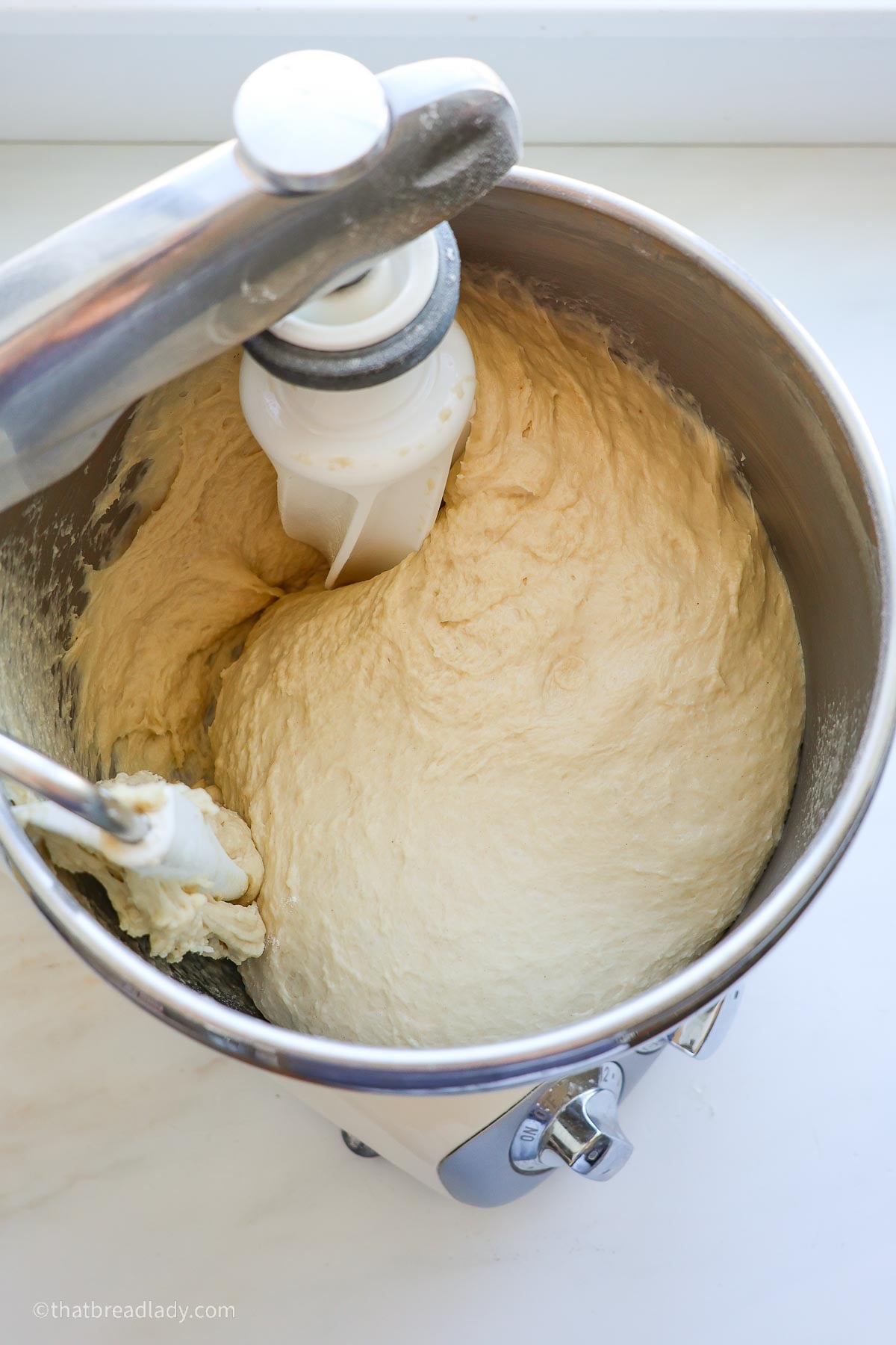 A stand mixer with a stainless steel bowl containing mixed roll dough.