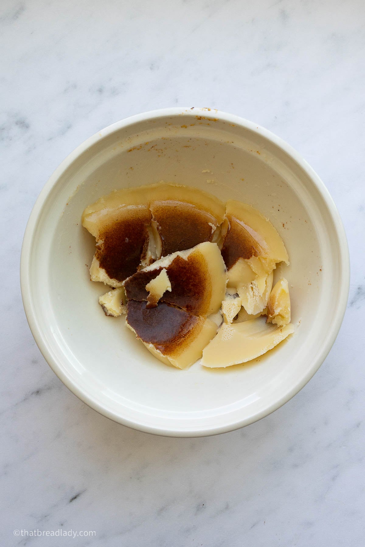 A bowl of chilled brown butter, broken into pieces, with brown flecks on the bottom of the butter pieces.
