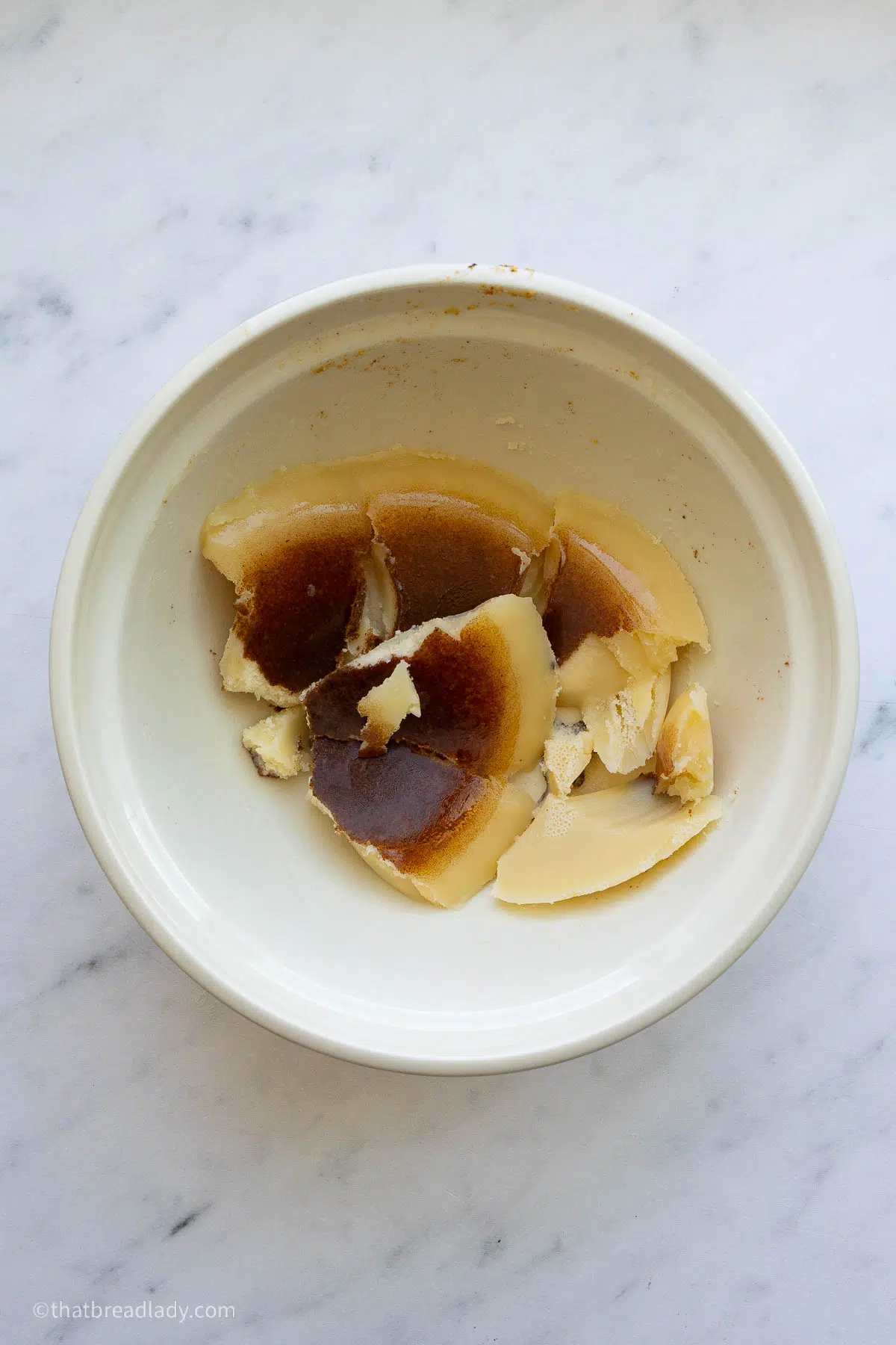 A bowl of chilled brown butter, broken into pieces, with brown flecks on the bottom of the butter pieces.