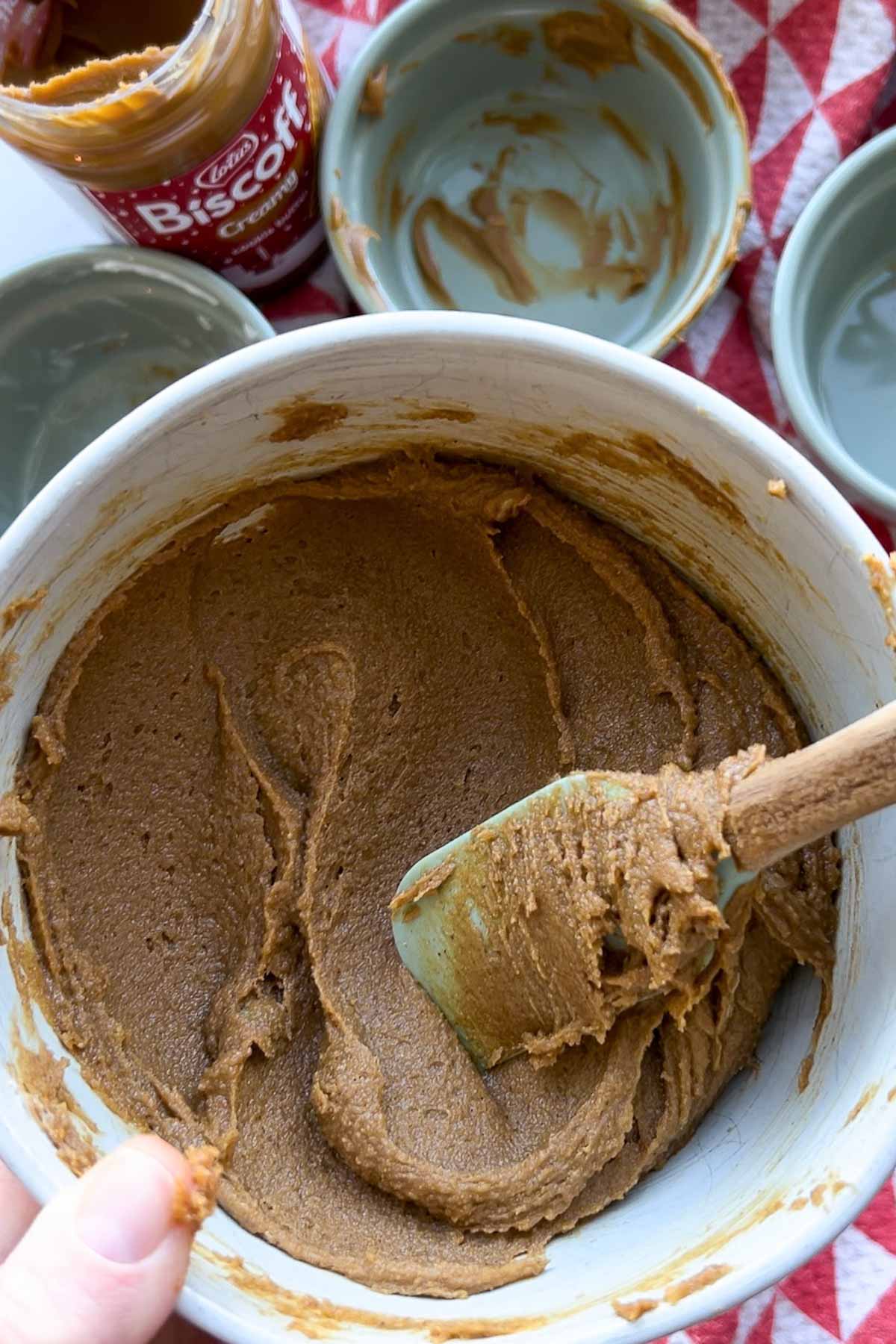 A bowl of biscoff cinnamon roll filling, with a silicone spatula stirring it.