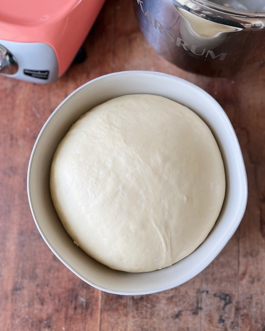 A bowl of risen dough, filling the bowl, and a stand mixer and stainless steel bowl.