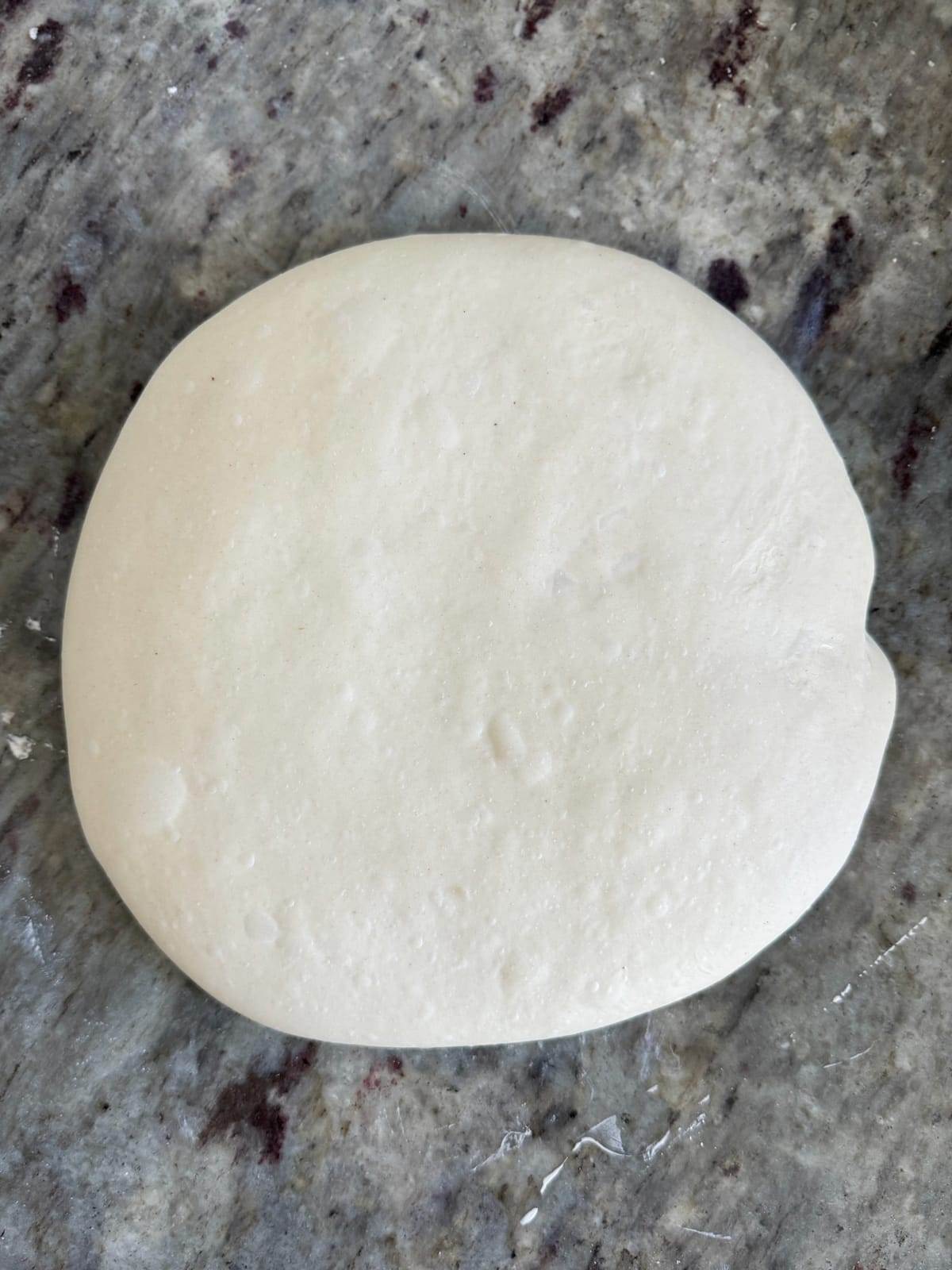 A round piece of sourdough dough resting on a gray marble countertop.