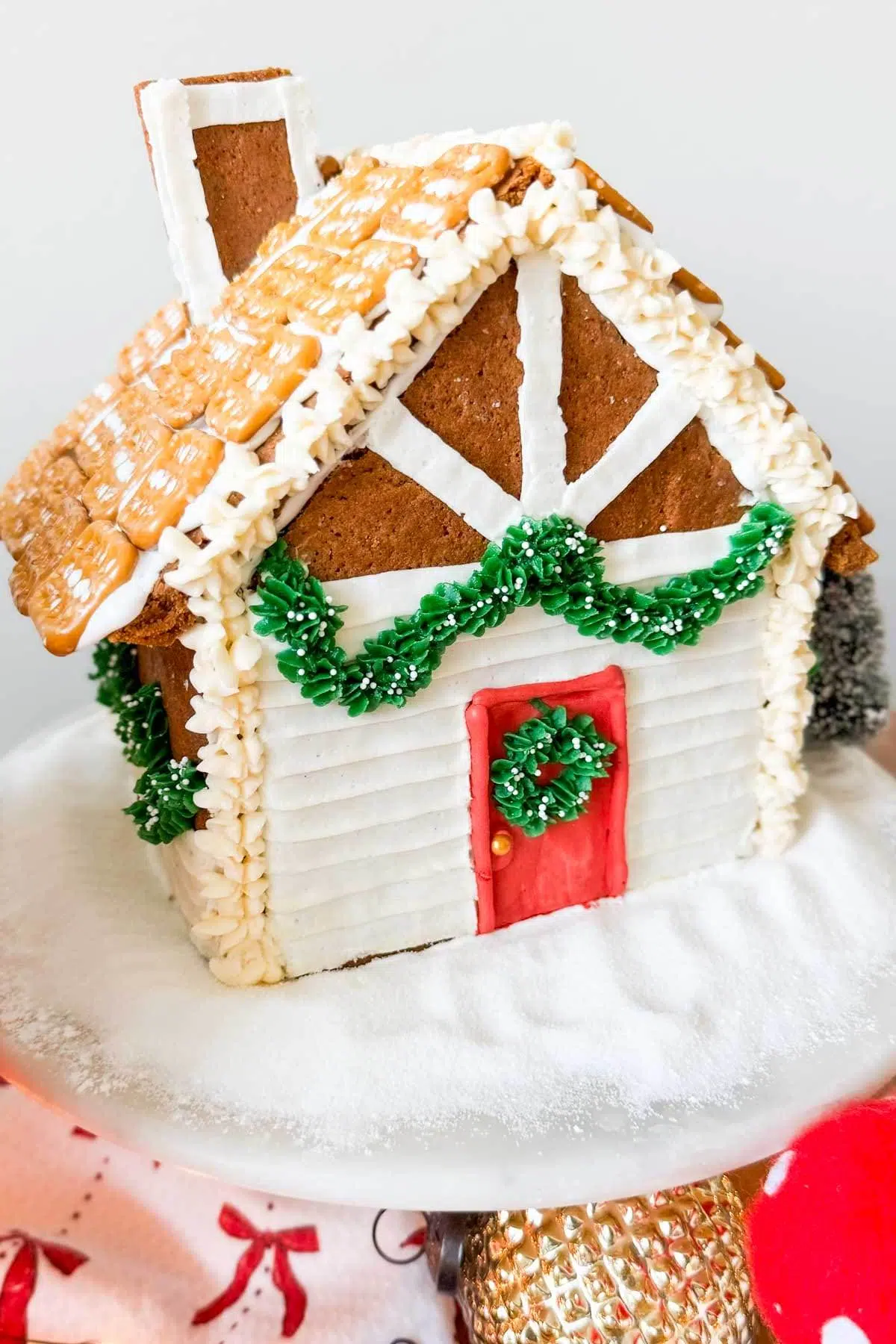 A gingerbread house decorated with pretzels squares on the roof, frosting garland across the front, and frosting siding on the front and sides.
