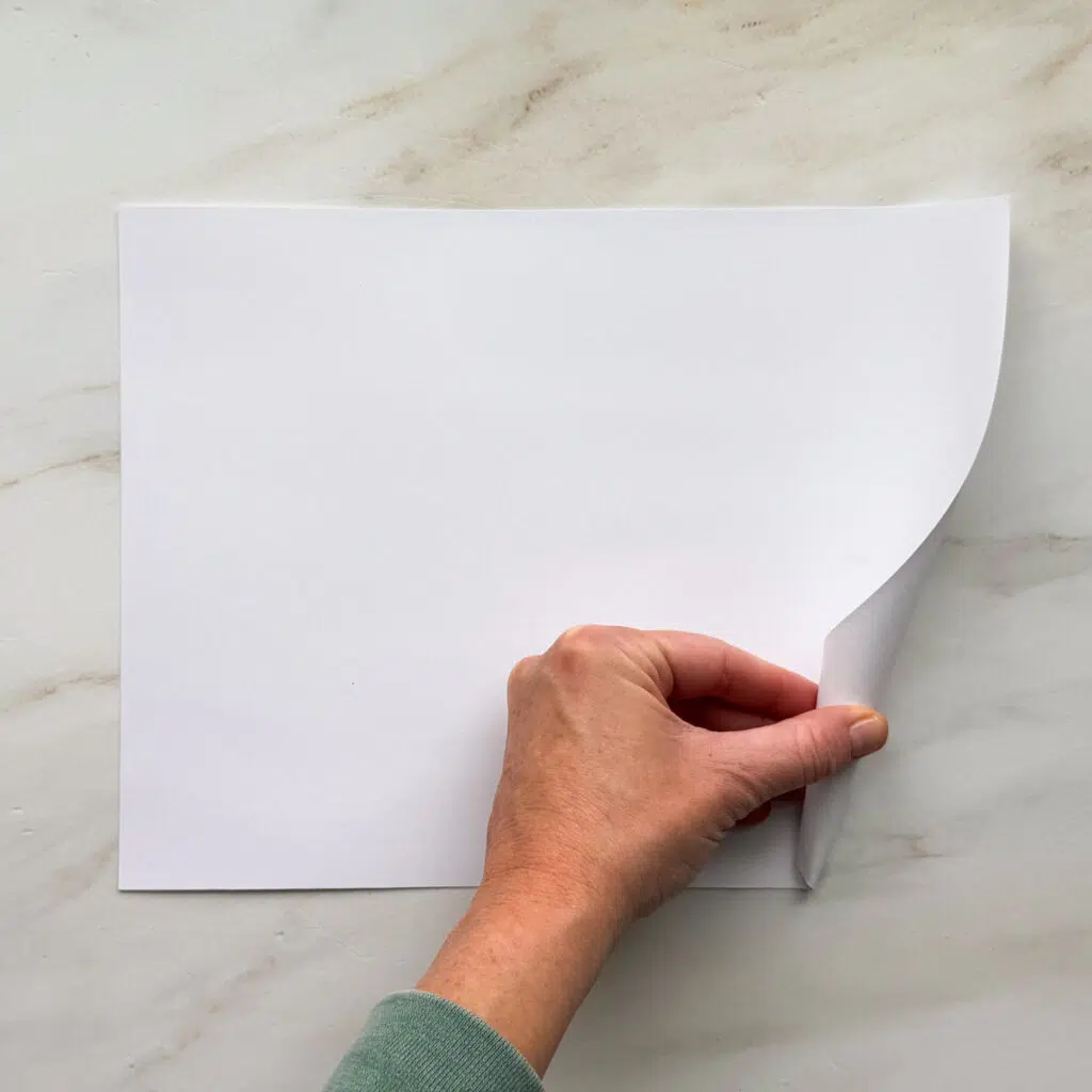 A hand rolling up a white 8.5 by 11-inch piece of paper.