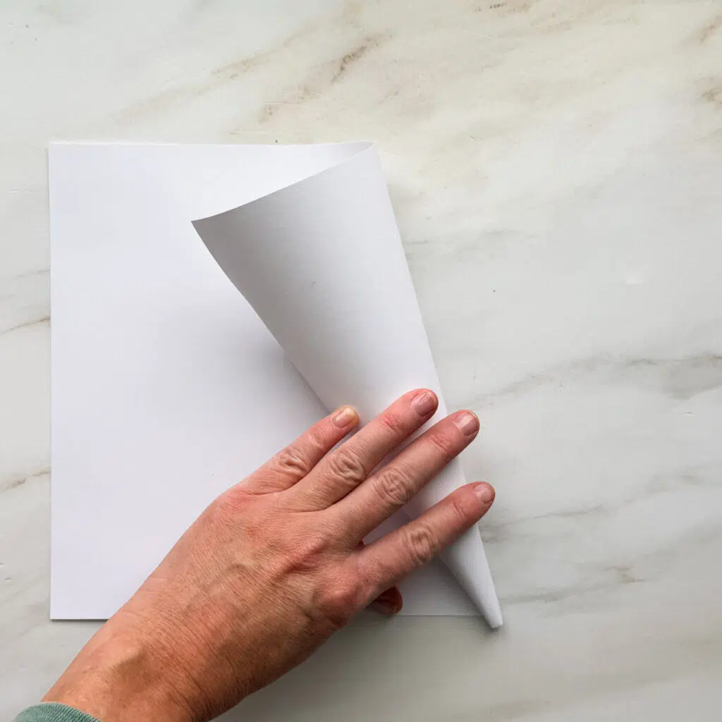 A hand rolling up a white 8.5 by 11-inch piece of paper.