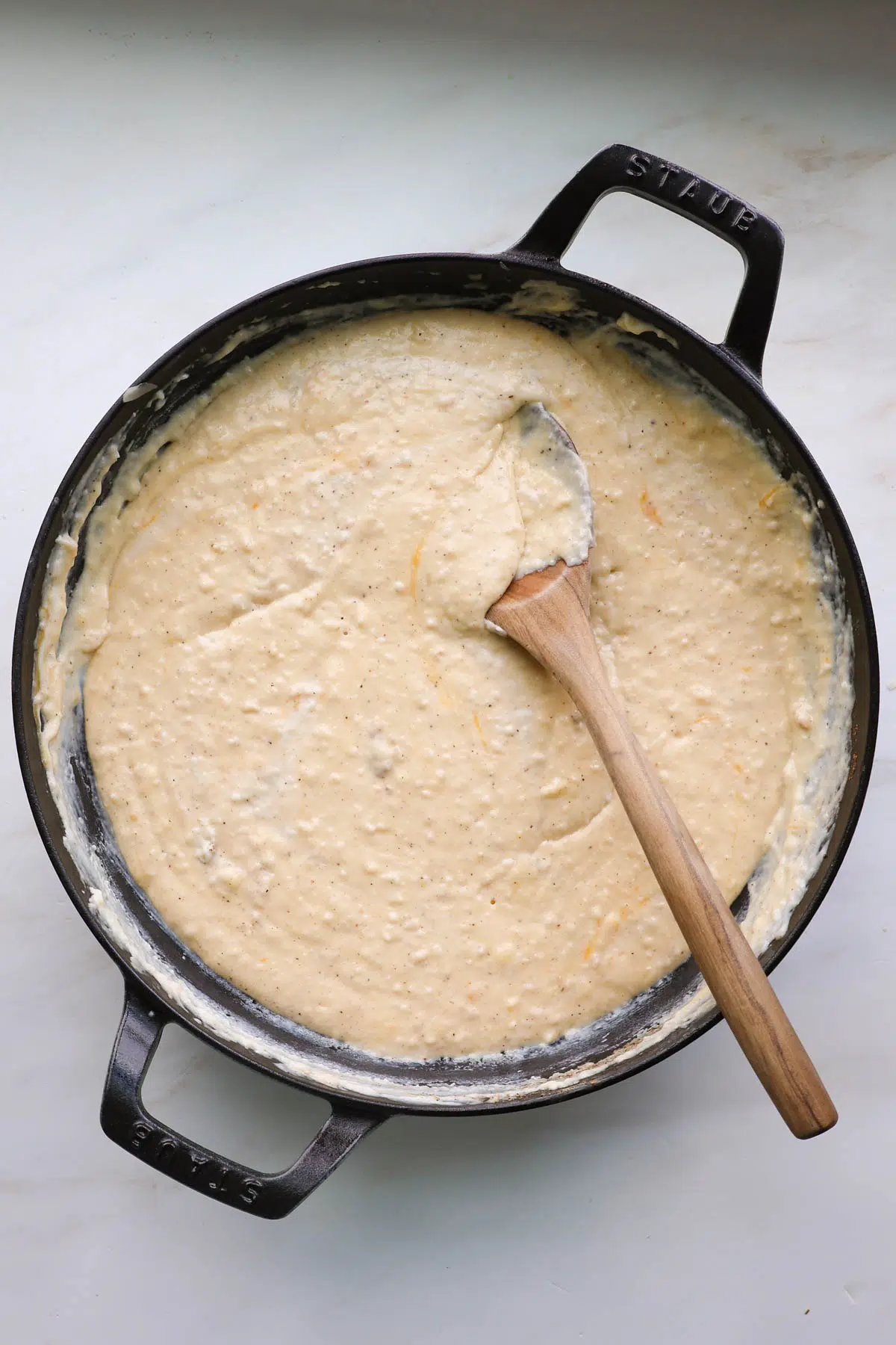 A cast iron pan with mac and cheese sauce with a wooden spoon.