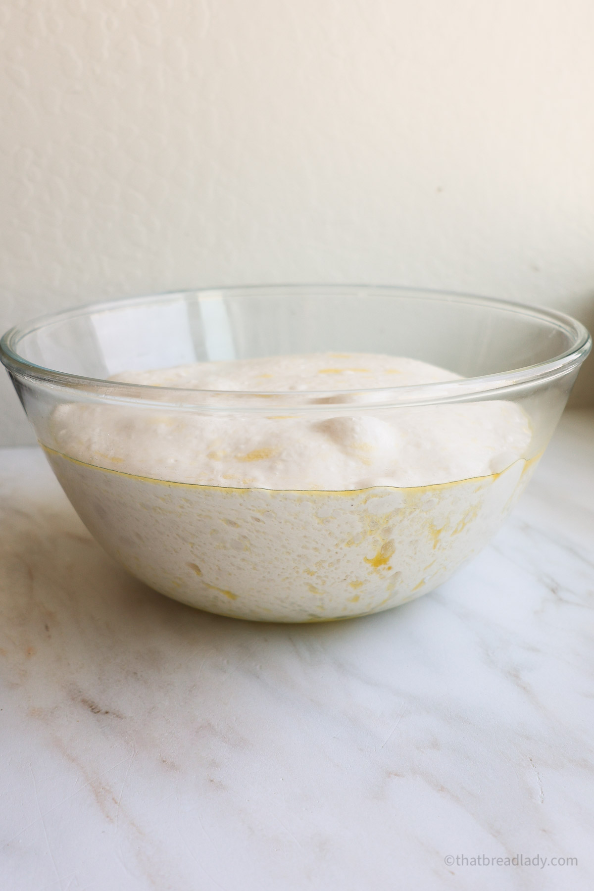 A glass bowl with risen focaccia dough in it.