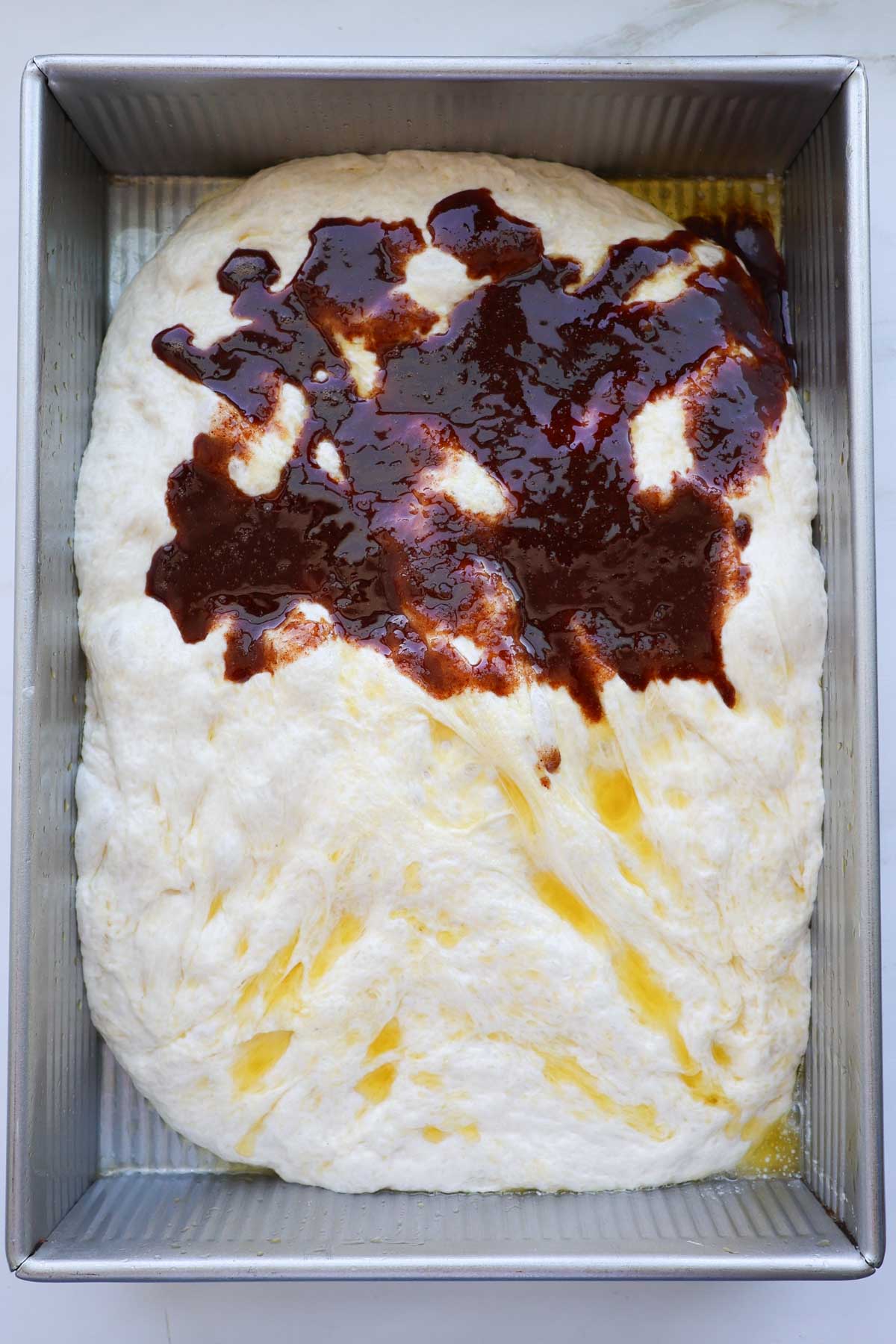 Focaccia dough in a pan with cinnamon sugar filling spread over the top half of it.