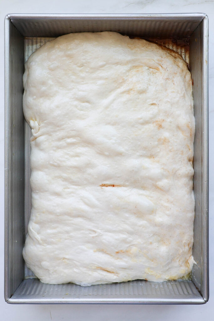 The focaccia dough spread out in the pan with cinnamon sugar filling inside.