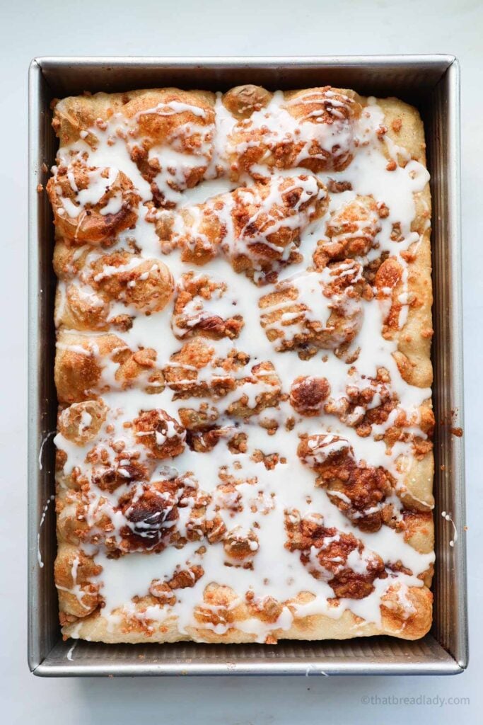 A pan of baked cinnamon roll focaccia with vanilla icing drizzled over it.