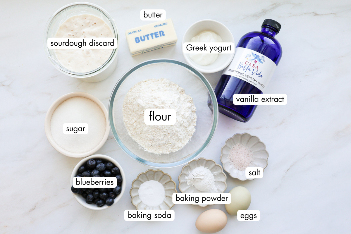 All the ingredients for the sourdough discard blueberry muffins measured out and sitting on a white marble countertop.