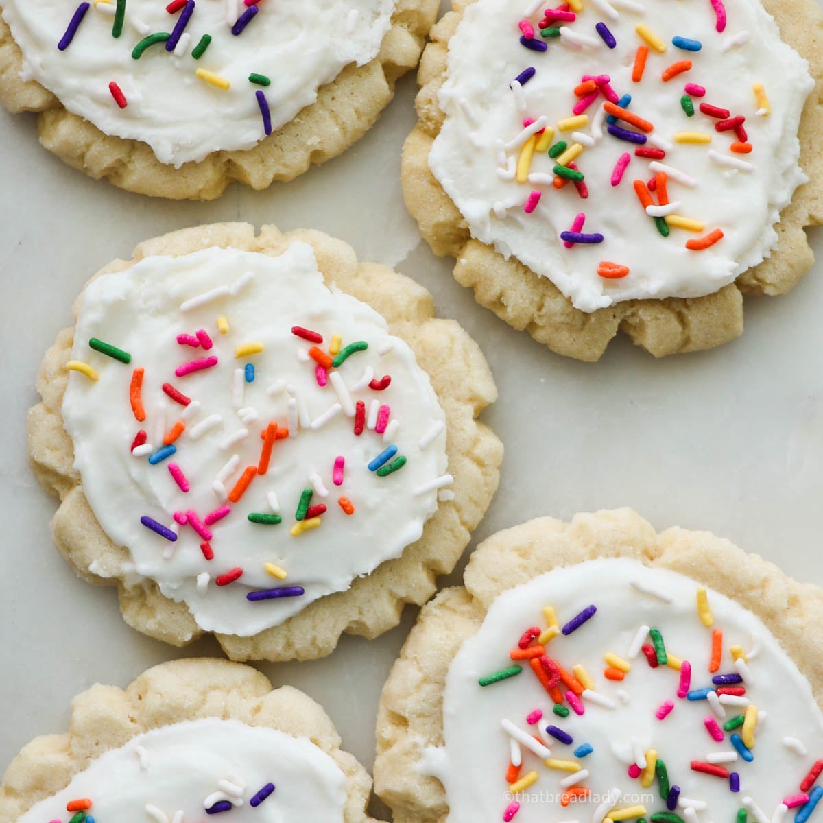 Several sourdough sugar cookies with white frosting and colorful sprinkles.