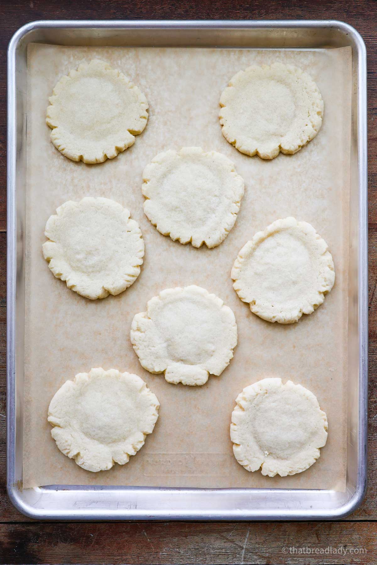 A baking sheet lined with parchment paper with 8 baked sourdough sugar cookies.