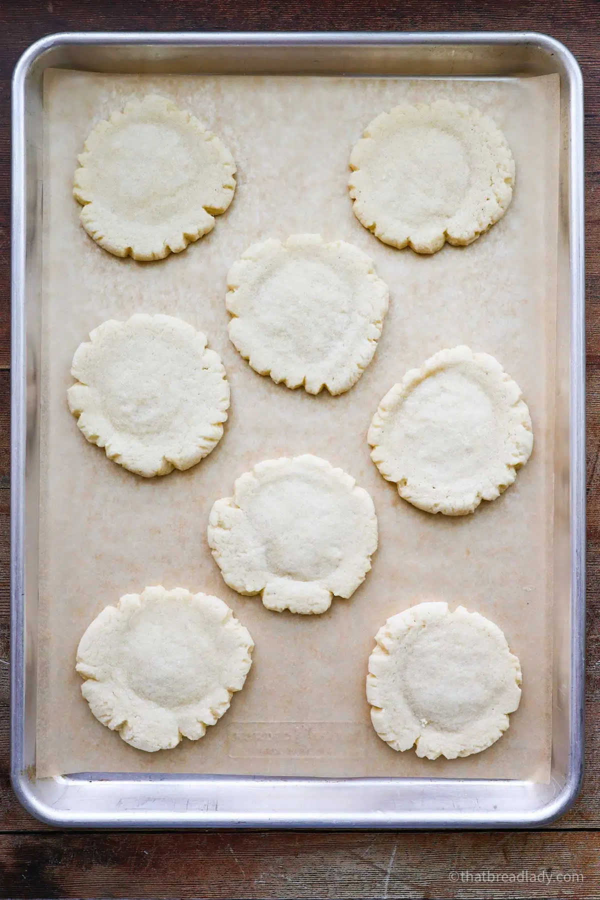 A baking sheet lined with parchment paper with 8 baked sourdough sugar cookies.