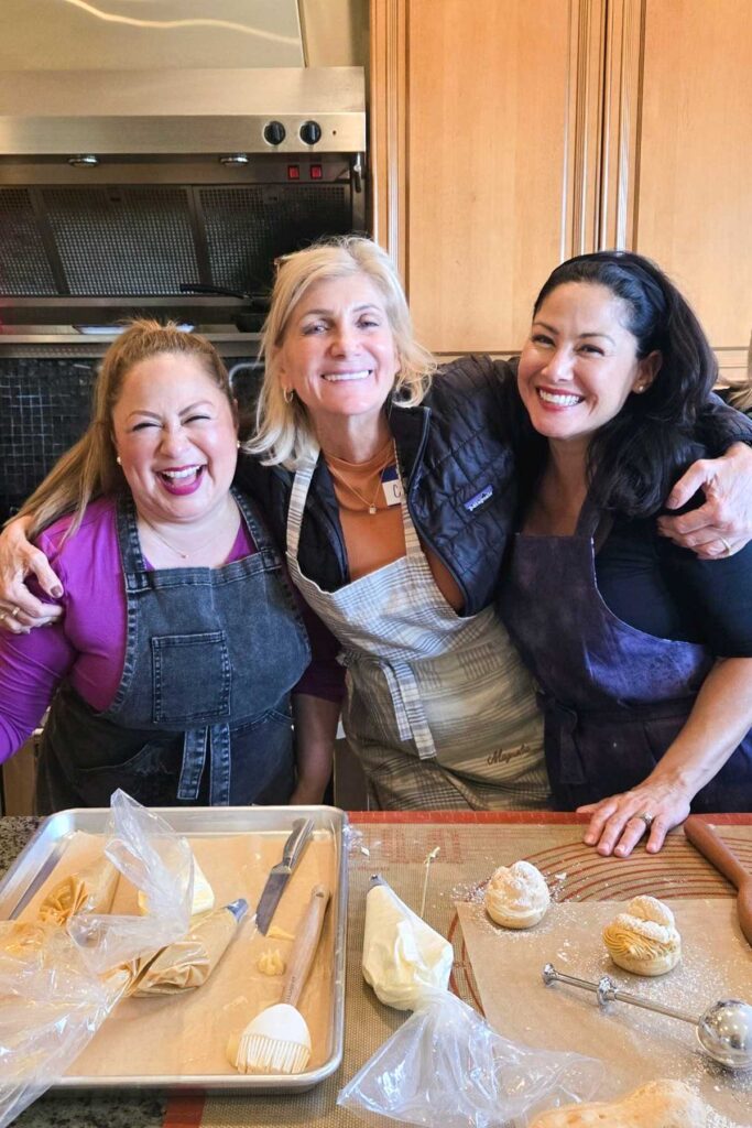 Three women at Heather's baking retreat, hugging and smiling in the kitchen.