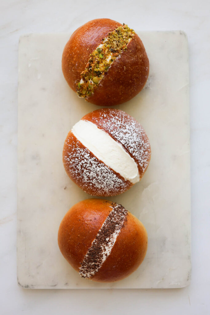 Three maritozzi buns on a white marble cutting board.