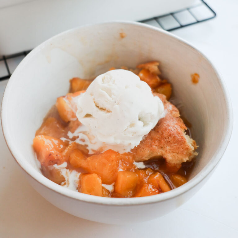 A bowl of sourdough peach cobbler with a scoop of vanilla ice cream on top.