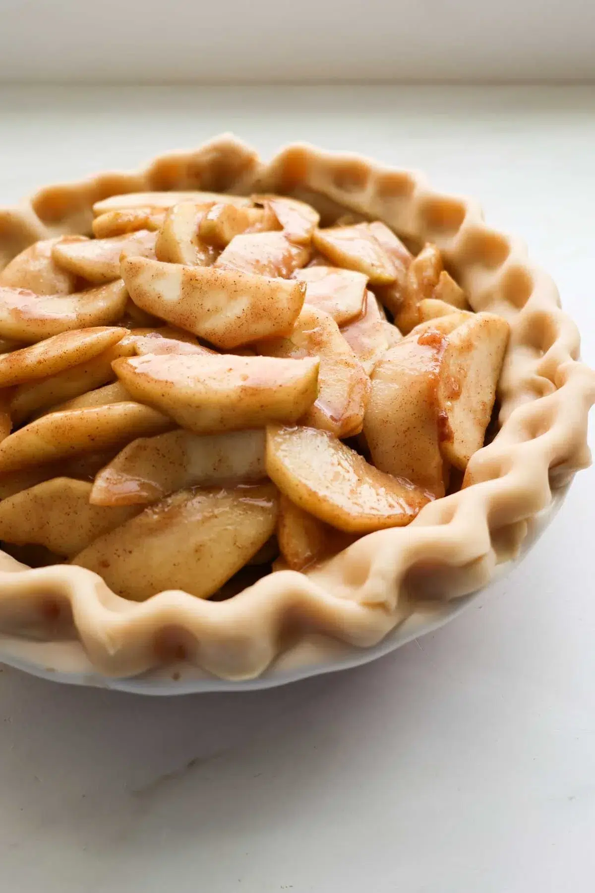 An unbaked apple pie, with the apples inside the pie crust and the edges are crimped.