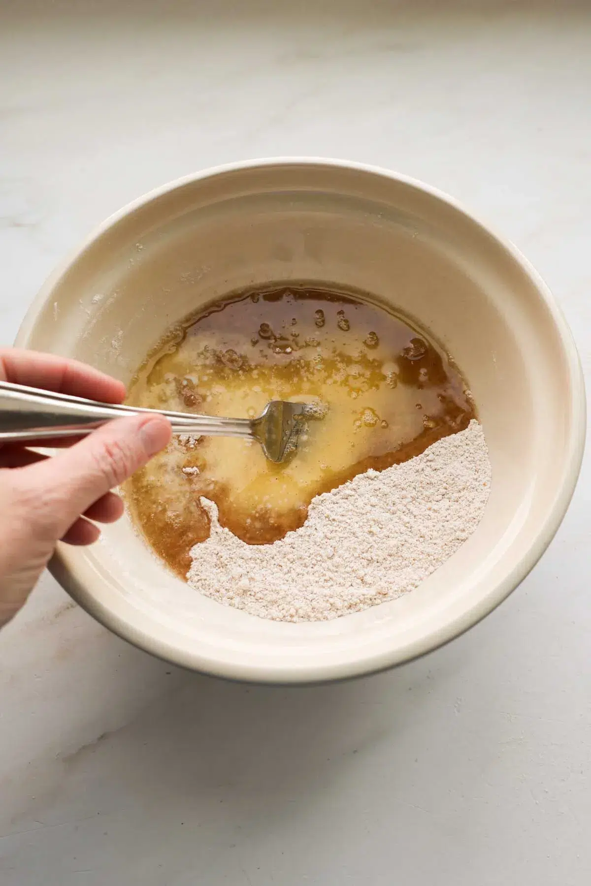 A bowl of unmixed ingredients for the crumb topping for apple pie, with a hand holding a fork, stirring it.
