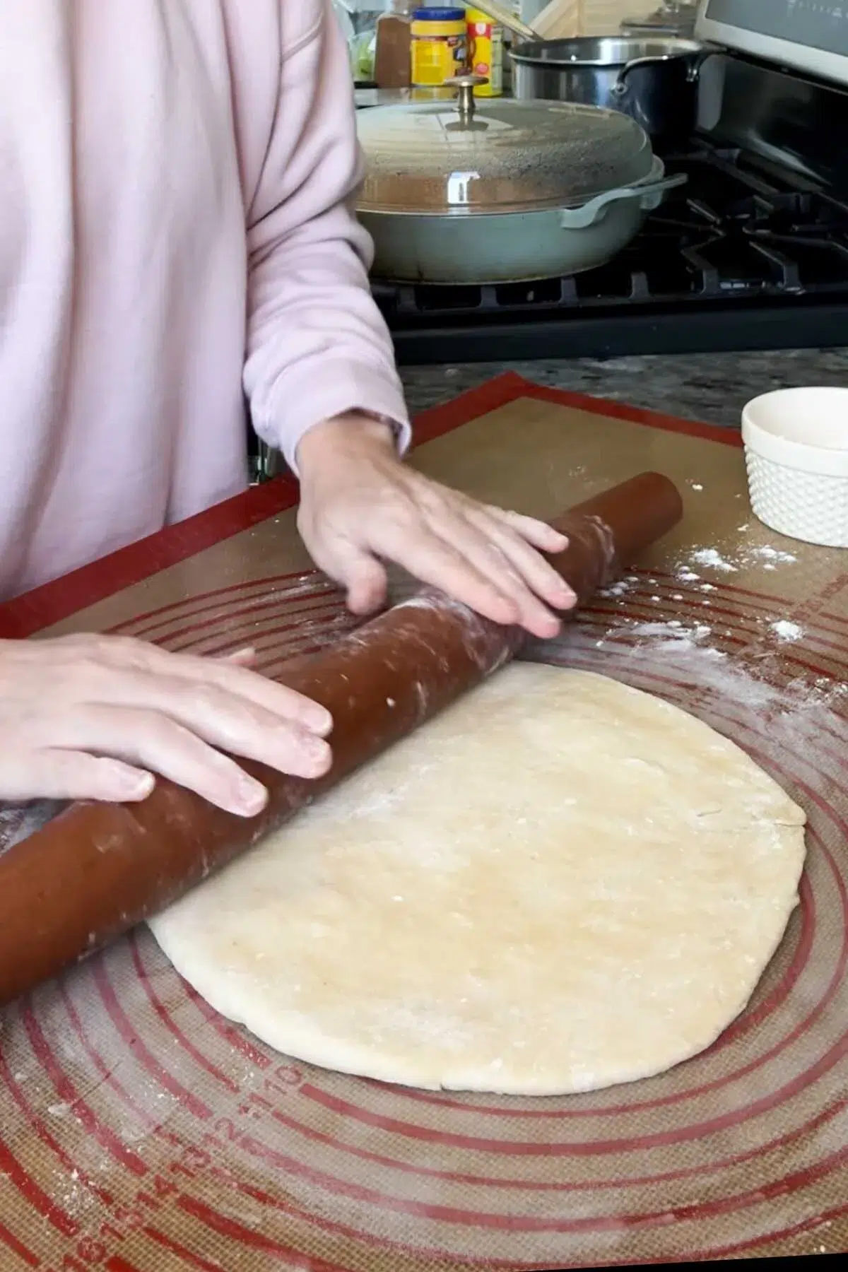 Two hands on a rolling pin, rolling out a pie crust on a silicone rolling mat.