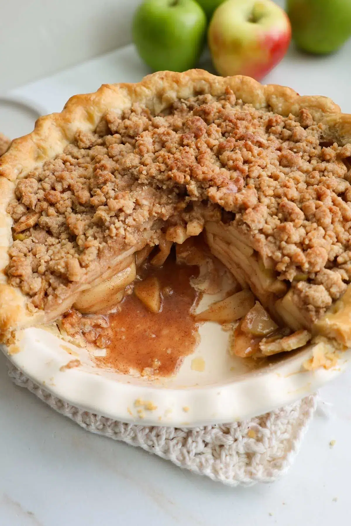 A baked apple crumble pie, with one slice missing, showing the layers of cinnamon apples inside.