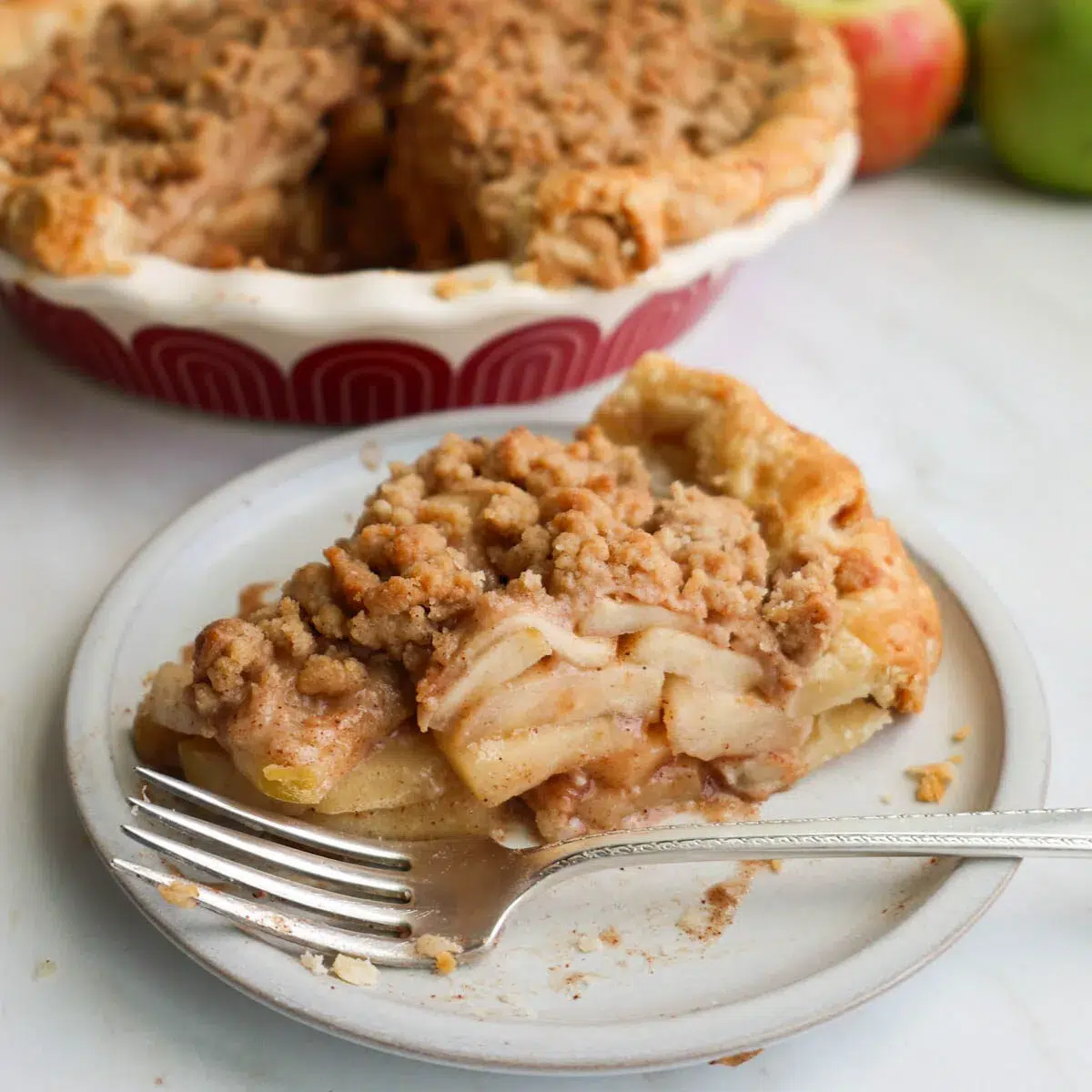 A slice of apple crumble pie, on a dessert plate, with a fork.