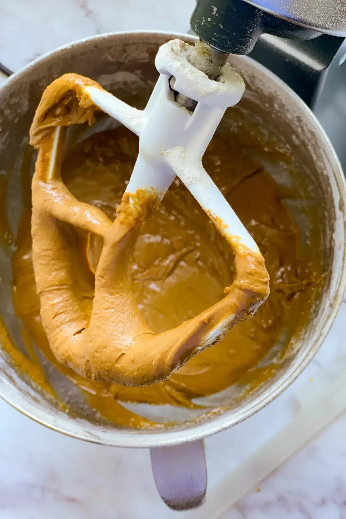 A stand mixer with a paddle attachment, above the gingerbread house mixture, after the flour has been incorporated.