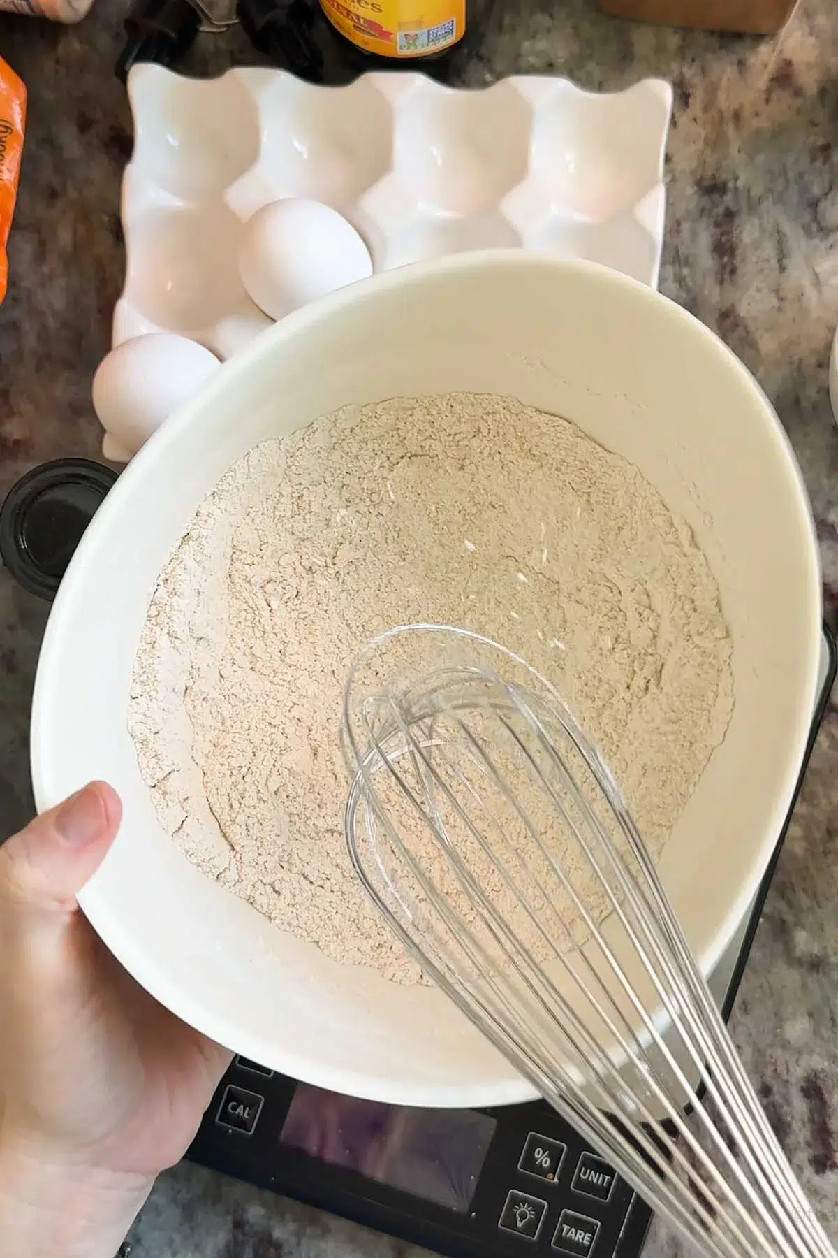 A bowl with the flour, salt, baking powder, cinnamon, ginger, and cloves being mixed together with a wire whisk.