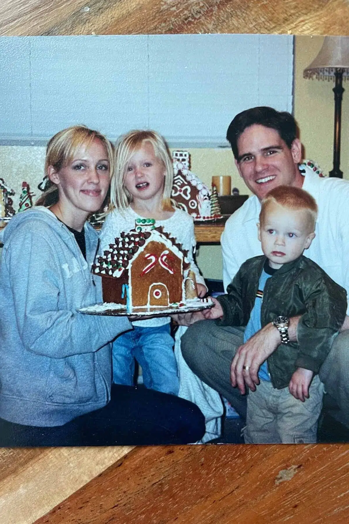 Heather, with her husband and two young children, holding a homemade gingerbread house.