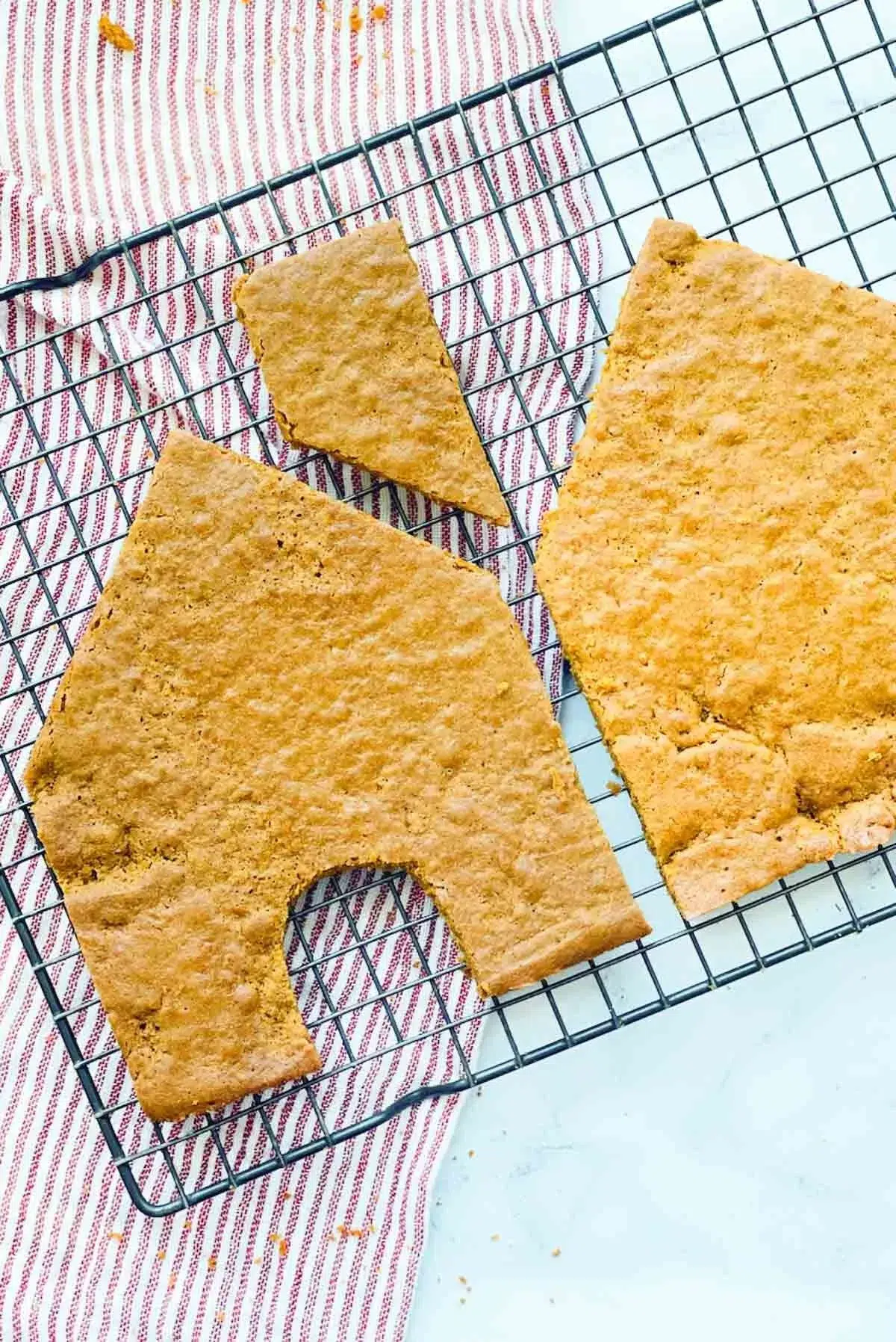 The front, chimney and back pieces of the gingerbread house, resting on a wire cooling rack, with a towel underneath.