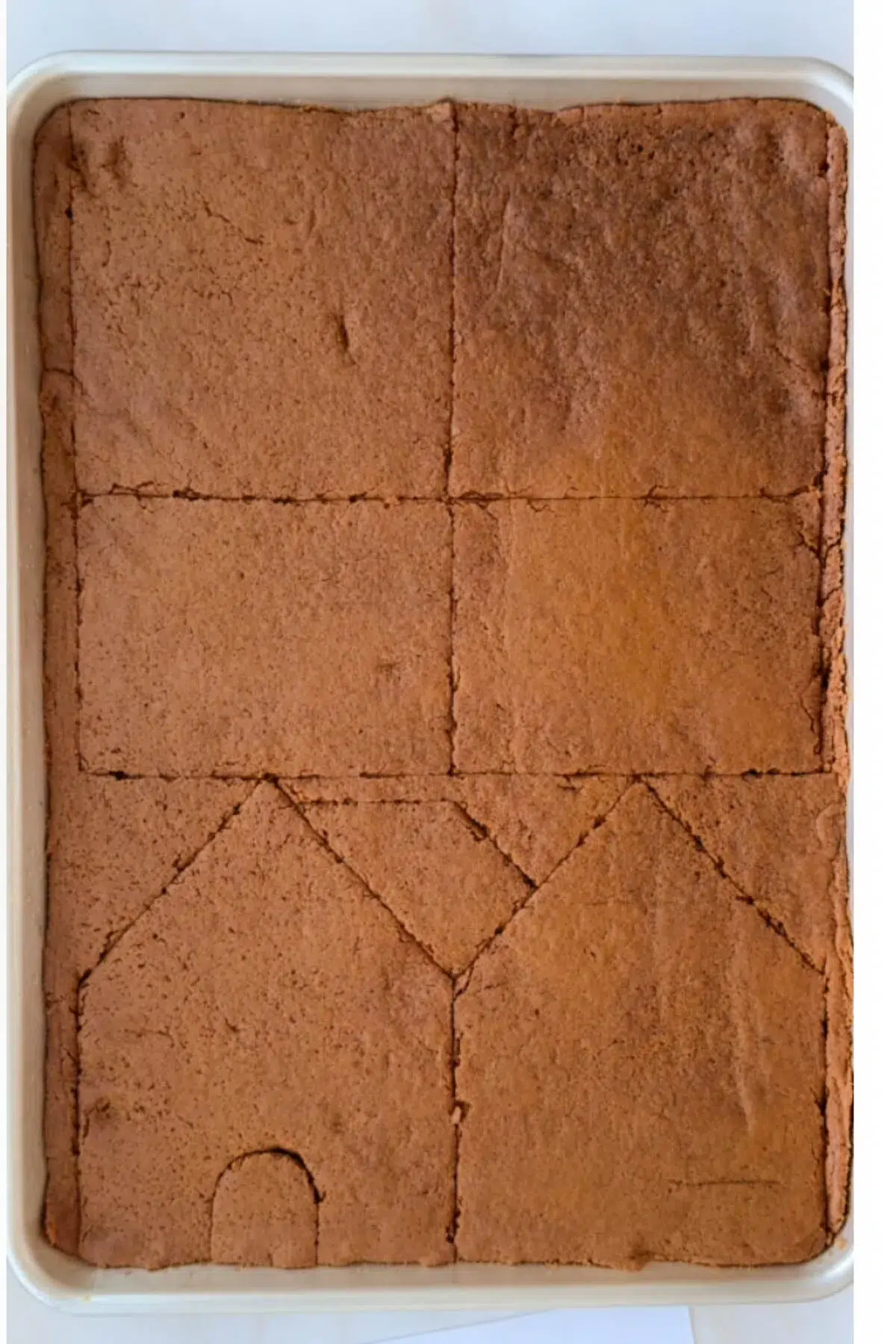 A sheet pan full of baked gingerbread, which has the outlines of gingerbread cutouts in it.