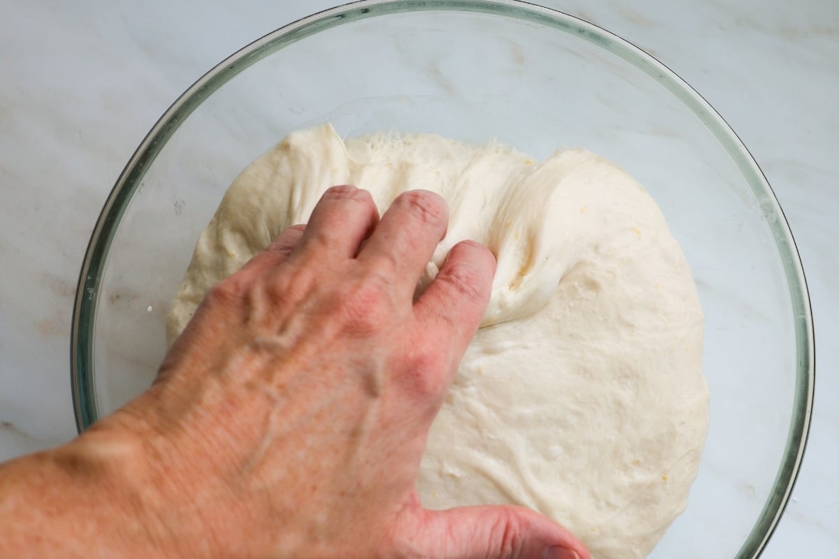 A hand pulling risen sourdough away from a glass bowl.