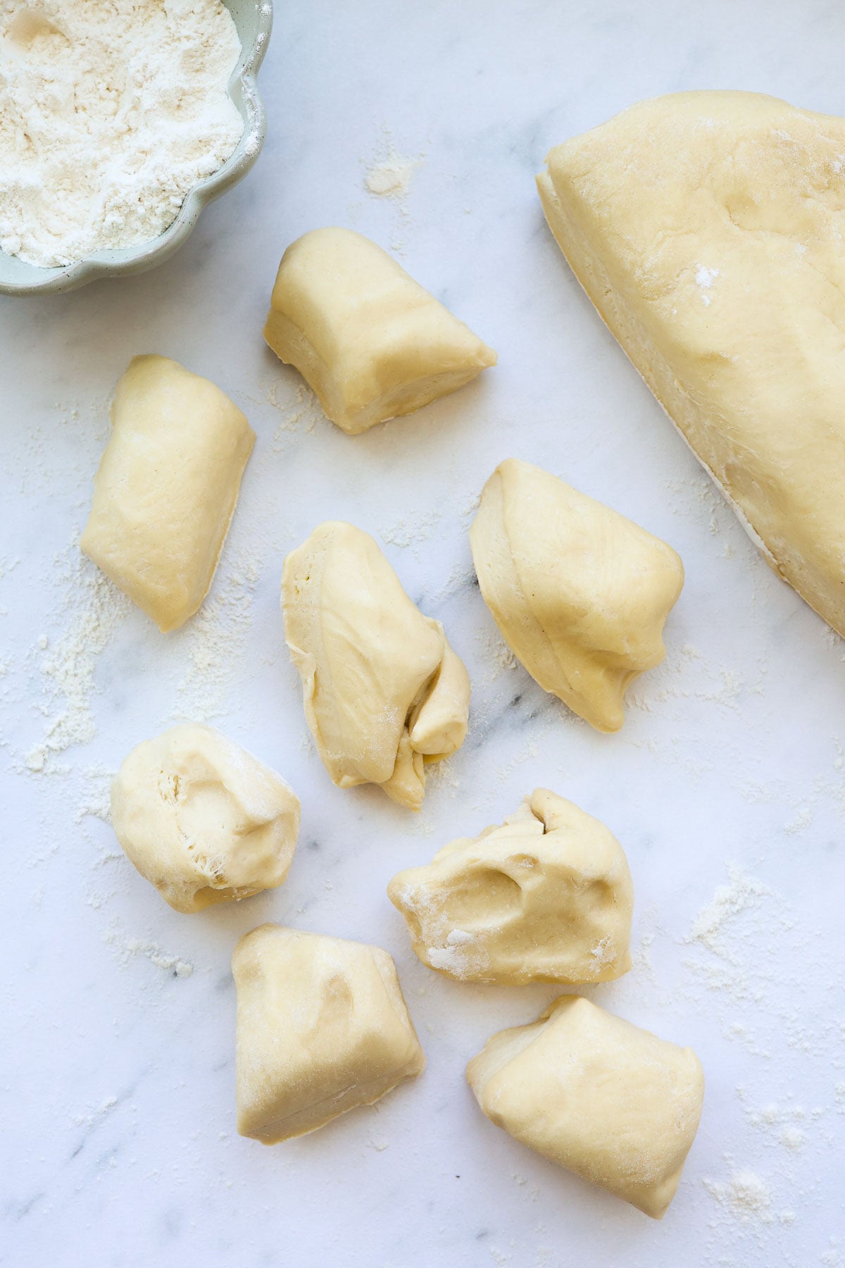 Several pieces of brioche dough divided, with a bowl of flour.