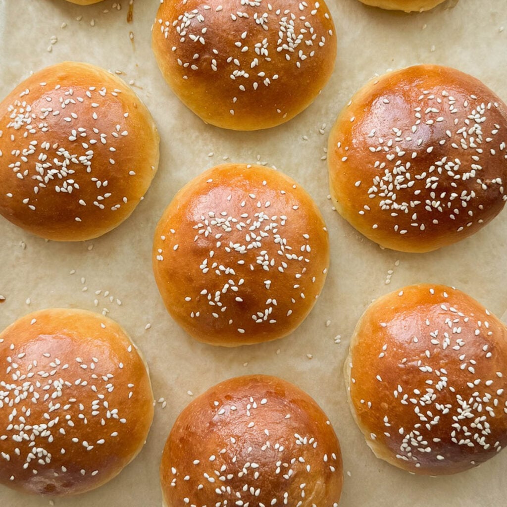 Several brioche hamburger buns with sesame seeds on top.