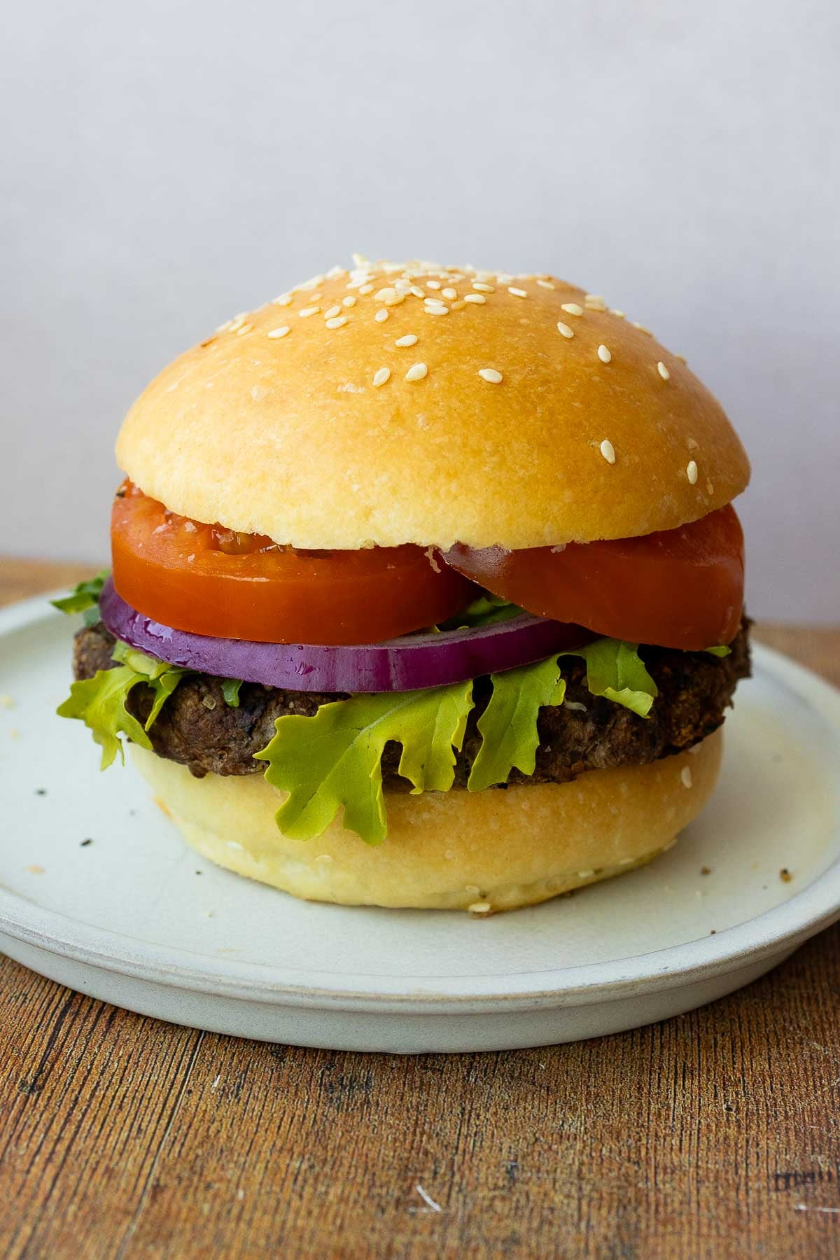 A hamburger with a brioche hamburger bun, sliced tomatoes, arugula, onion, and a hamburger patty, on a plate.