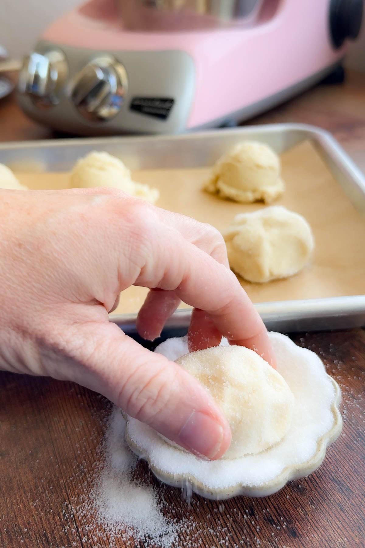 A hand holding a ball of swig cookie dough, dipping it in a bowl of granulated sugar.