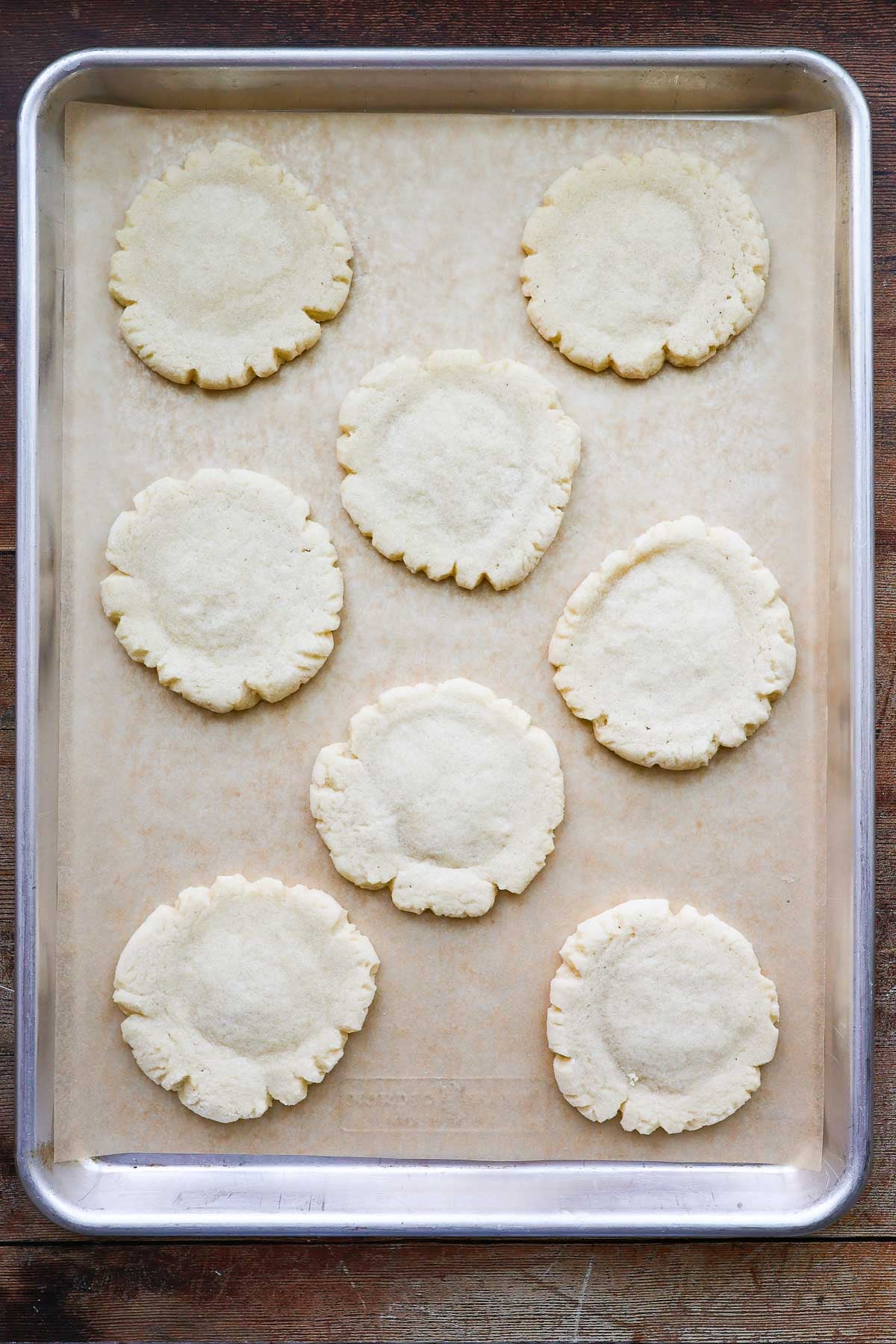 A parchment lined baking sheet with 8 baked, unfrosted swig cookies.
